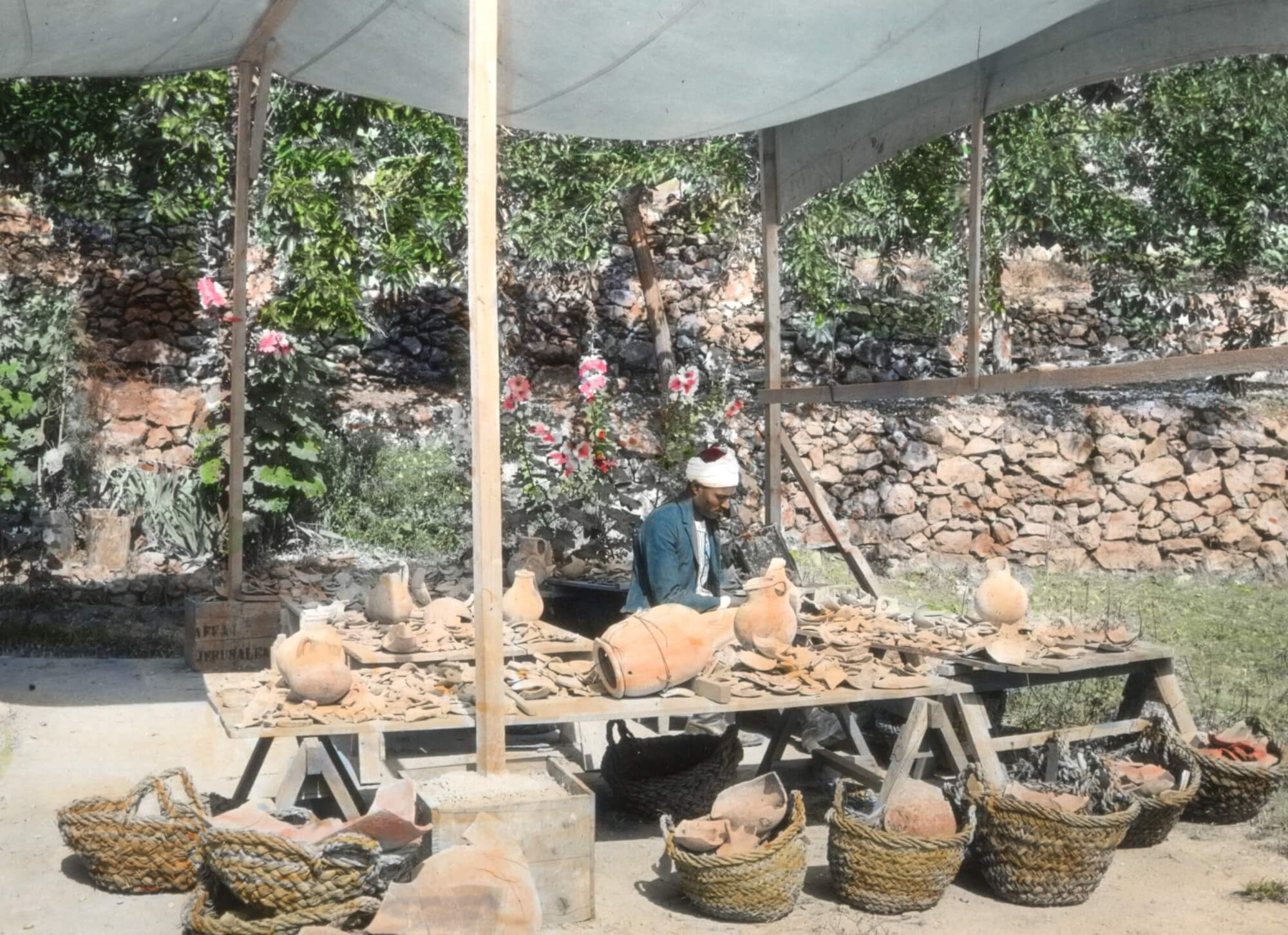 Figure 7. Reis Mahmoud Kureyim restoring pottery on the terrace of Maloufiya, 31 May 1929. Badè Museum photographic archive 371 N P.I. 469. Colorized lantern slide. Courtesy of the Badè Museum, Pacific School of Religion.