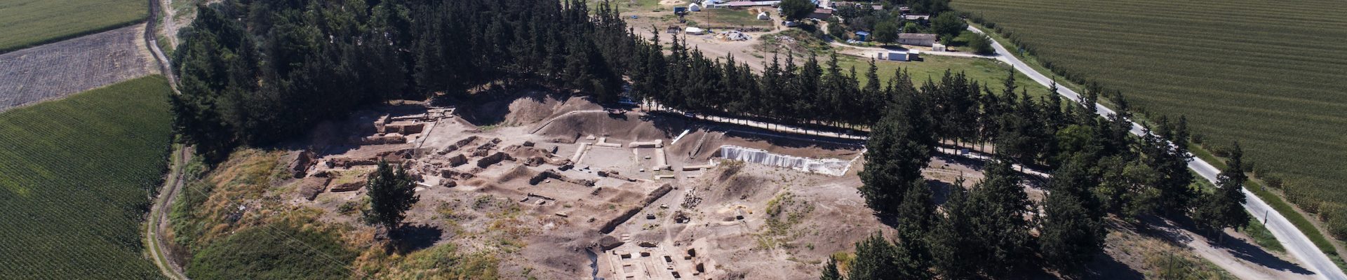 Figure 1: Tell Atchana, ancient Alalakh viewed from the northwest. In the foreground is the Level VII City Gate, where mudbricks are being dried in the sun. The palace and temple area excavated in the 1930s and 1940s is surrounded by trees, beyond which lie further excavation areas, and modern-day farms and villages.