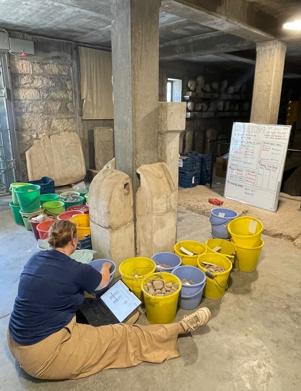I am sitting with my buckets and whiteboard, updating the information for the unwashed shell and bone on my spreadsheet. Photo by James Razumoff