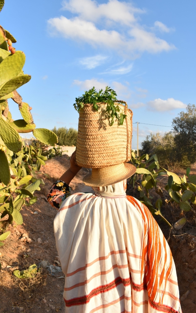 A DJERBIAN WOMAN IN TRADITIONAL DRESS CARRYING A BASKET ON HER HEAD | إمرأة جربية باللباس التقليدي تحمل قفة فوق رأسها