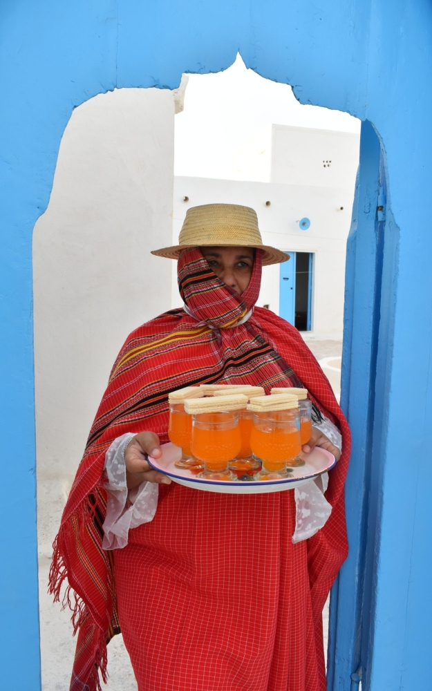 A woman in Djerba's daily dress in front of a Djerban house | إمرأة بلباس جربة اليومي أمام باب حوش جربي
